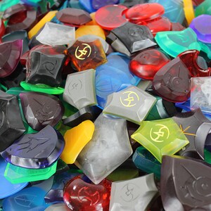 Puede incluir: Una colecci&oacute;n de piezas de juego de pl&aacute;stico transparente de varios colores, formas y tama&ntilde;os. Algunas piezas tienen un s&iacute;mbolo de rayo y el n&uacute;mero 25.