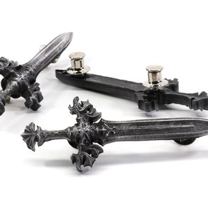 May include: Three silver-toned sword pins with intricate details. Each pin has a black metal base and a silver-toned pin back.