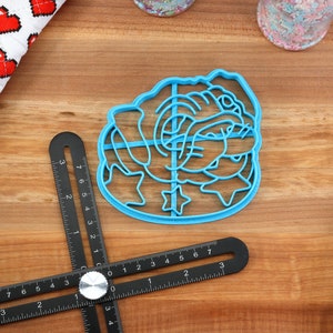 May include: A blue plastic cookie cutter shaped like a cartoon bulldog with stars around it.