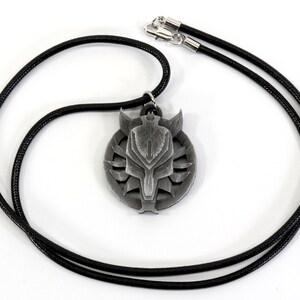 Op de afbeelding: Een zilveren ketting met een hanger in de vorm van een wolfskop. De hanger is rond en heeft een zwart leren koord.