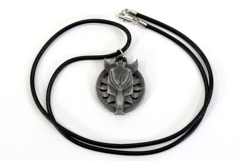 Op de afbeelding: Een zilveren ketting met een hanger in de vorm van een wolfskop. De hanger is rond en heeft een zwart leren koord.