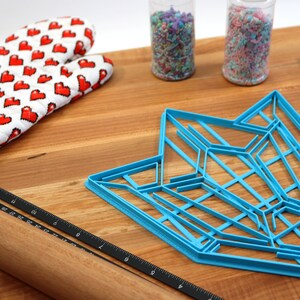Puede incluir: Un cortador de galletas de pl&aacute;stico azul en forma de estrella geom&eacute;trica, un rodillo de madera, un guante de horno rojo y blanco y dos frascos de chispas en una superficie de madera.