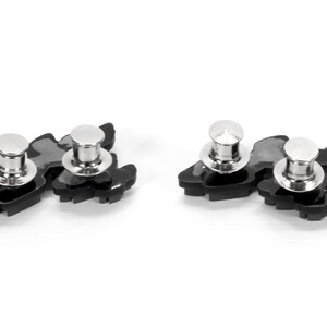 May include: Two black metal pinback buttons with silver metal posts. Each button features a stylized design of a bird with its wings spread.