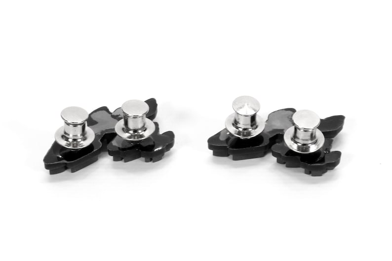 May include: Two black metal pinback buttons with silver metal posts. Each button features a stylized design of a bird with its wings spread.