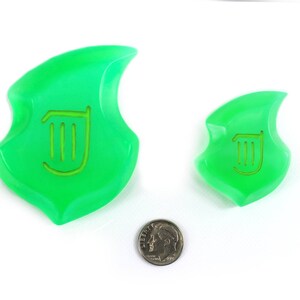 May include: Two green plastic game pieces shaped like a stylized leaf with a harp symbol in the center. The larger piece is about the size of a US quarter.