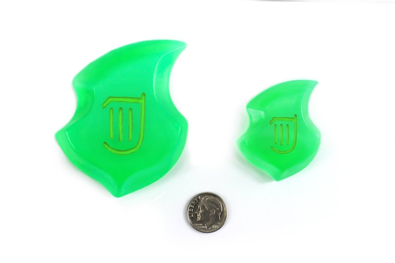 May include: Two green plastic game pieces shaped like a stylized leaf with a harp symbol in the center. The larger piece is about the size of a US quarter.