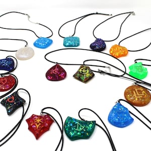 May include: A collection of 14 necklaces with various colored resin pendants featuring different symbols. The pendants are iridescent and have a glittery finish. The necklaces are all black.