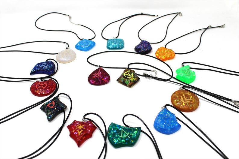 May include: A collection of 14 necklaces with various colored resin pendants featuring different symbols. The pendants are iridescent and have a glittery finish. The necklaces are all black.