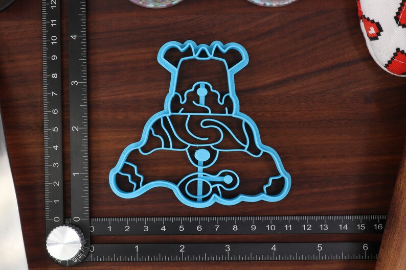 May include: A blue plastic cookie cutter shaped like a snowman with a hat and a scarf. The cutter has a detailed design with wavy lines and circles.