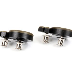 May include: Two black and green plastic buttons with silver metal posts. The buttons are shaped like a rounded rectangle with a slight curve.