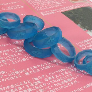 May include: A stack of blue silicone rings with raised numbers and symbols on a pink surface. The rings are stacked in a random order.