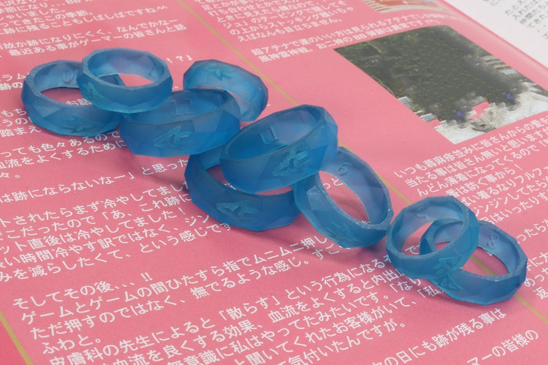 May include: A stack of blue silicone rings with raised numbers and symbols on a pink surface. The rings are stacked in a random order.