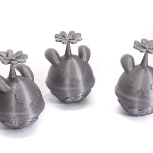 May include: Three gray 3D printed figurines with a flower on top. Each figurine has a round body with bunny ears and a face.