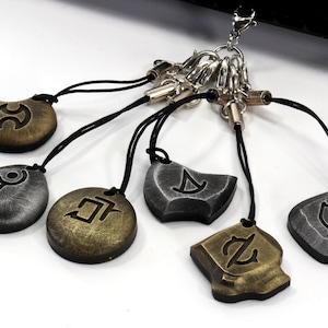 Może przedstawiać: Zestaw siedmiu brelok&oacute;w z r&oacute;żnymi symbolami na każdym. Breloki są wykonane z metalu i mają czarny sznurek. Symbole to koło z linią przechodzącą przez nie, koło z linią przechodzącą przez nie i kropką, koło z linią przechodzącą przez nie i kropką i linią, koło z linią przechodzącą przez nie i kropką i linią i k&oacute;łkiem, koło z linią przechodzącą przez nie i kropką i linią i k&oacute;łkiem i linią, koło z linią przechodzącą przez nie i kropką i linią i k&oacute;łkiem i linią i k&oacute;łkiem, oraz koło z linią przechodzącą przez nie i kropką i linią i k&oacute;łkiem i linią i k&oacute;łkiem i linią.