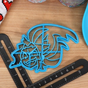 May include: A blue plastic cookie cutter shaped like a cartoon monster with a toothy grin and a large, wavy mane.
