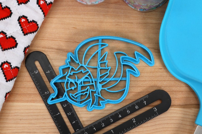 May include: A blue plastic cookie cutter shaped like a cartoon monster with a toothy grin and a large, wavy mane.