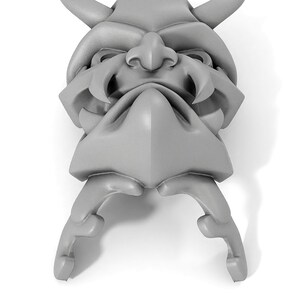 May include: A gray, detailed, 3D printed model of a demon mask with horns, fangs, and a furrowed brow.