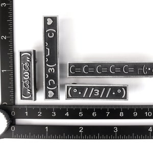 May include: Four silver metal stamp blocks with different designs. The designs include a heart, the text "(3)", the text "C=C=C=C=C= (;・&omega;・)", and the text "(.//3//0)".