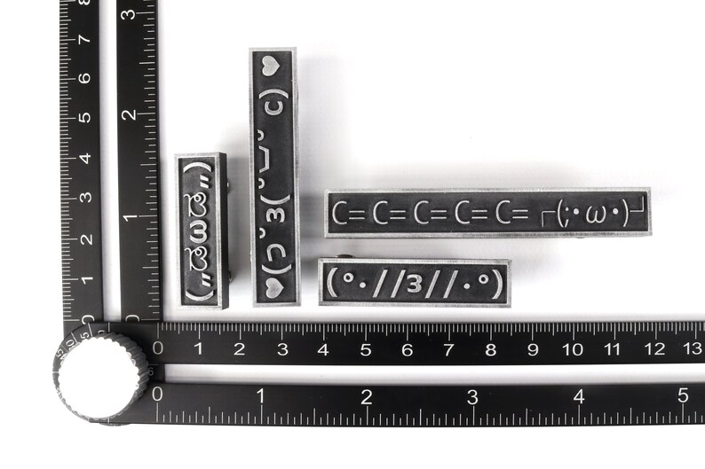 May include: Four silver metal stamp blocks with different designs. The designs include a heart, the text "(3)", the text "C=C=C=C=C= (;・&omega;・)", and the text "(.//3//0)".