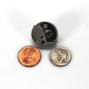 May include: A silver yin yang pin with a black and white design. The pin is surrounded by two US coins, a penny and a dime.