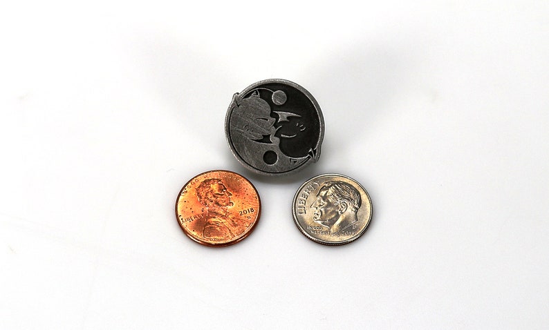May include: A silver yin yang pin with a black and white design. The pin is surrounded by two US coins, a penny and a dime.
