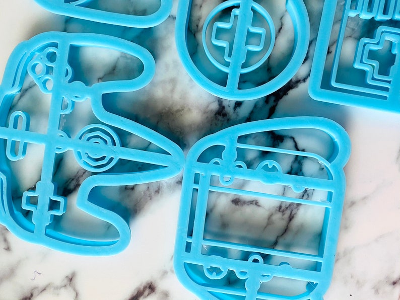 May include: A set of five blue plastic cookie cutters shaped like video game controllers and a game cartridge.