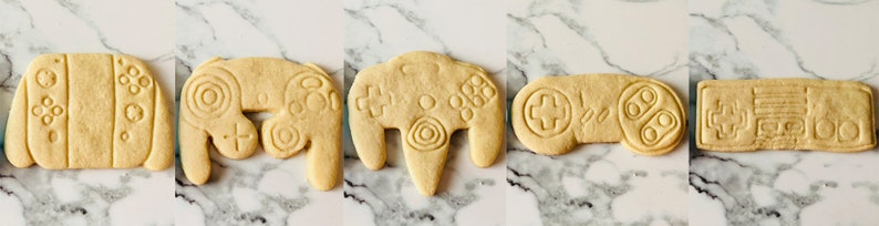 May include: Five different cookie cutters shaped like video game controllers. The cutters are made of a light brown dough and are ready to be baked.