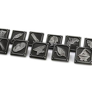 May include: A set of twelve silver-colored metal tokens with various symbols, including a crown, wheat, a hammer, a loaf of bread, an anvil, a helmet, a leaf, a fish, and a boat. The tokens are arranged in a row on a white background.