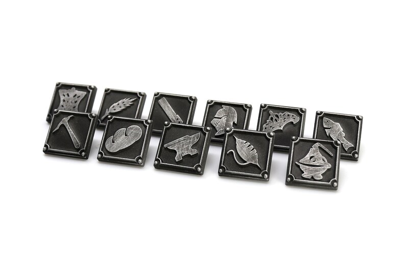 May include: A set of twelve silver-colored metal tokens with various symbols, including a crown, wheat, a hammer, a loaf of bread, an anvil, a helmet, a leaf, a fish, and a boat. The tokens are arranged in a row on a white background.