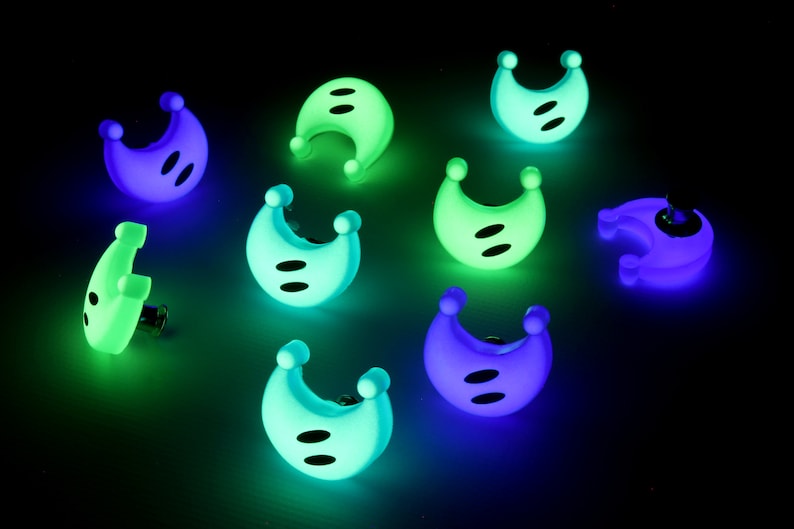 May include: Nine glow-in-the-dark plastic moon-shaped buttons in various shades of green, blue, and purple. The buttons have two black dots on each.
