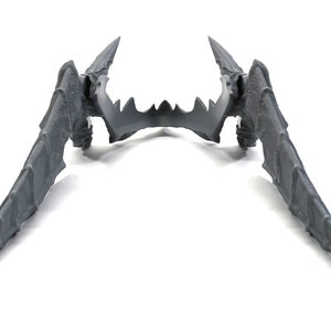 May include: A pair of grey plastic wings with a pointed tip and a textured surface. The wings are symmetrical and have a sharp, jagged edge.