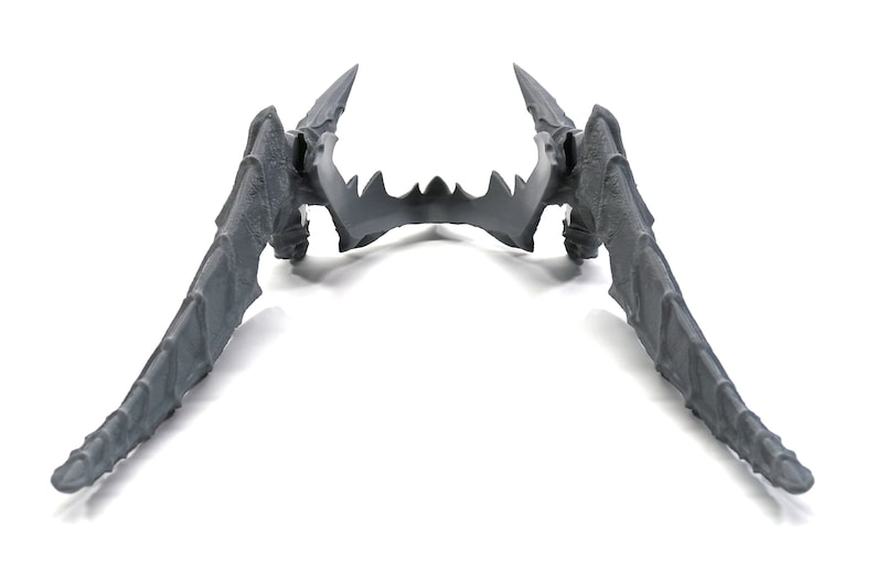 May include: A pair of grey plastic wings with a pointed tip and a textured surface. The wings are symmetrical and have a sharp, jagged edge.