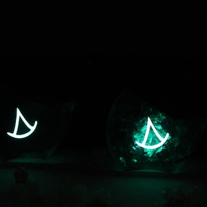 May include: Two glass containers with a teal glow, each containing a white sailboat design.