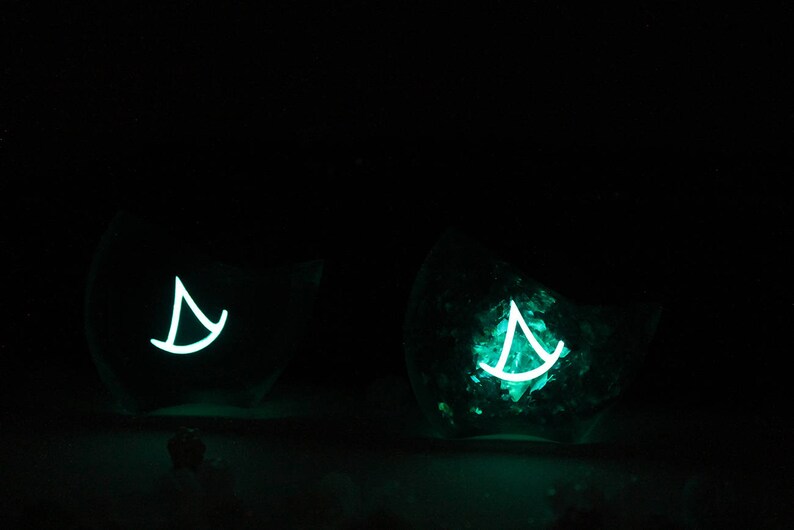 May include: Two glass containers with a teal glow, each containing a white sailboat design.