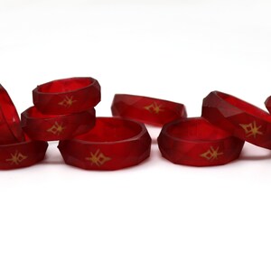 May include: A group of eight red silicone rings with a gold geometric design. The rings are stacked and scattered on a white surface.