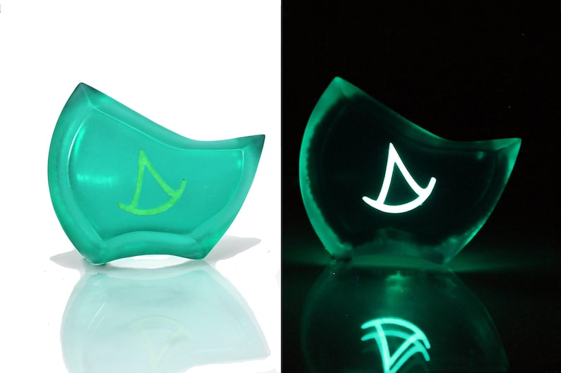 May include: A teal blue resin paperweight with a green glow-in-the-dark symbol of a sailboat inside. The paperweight is shaped like a crescent moon.
