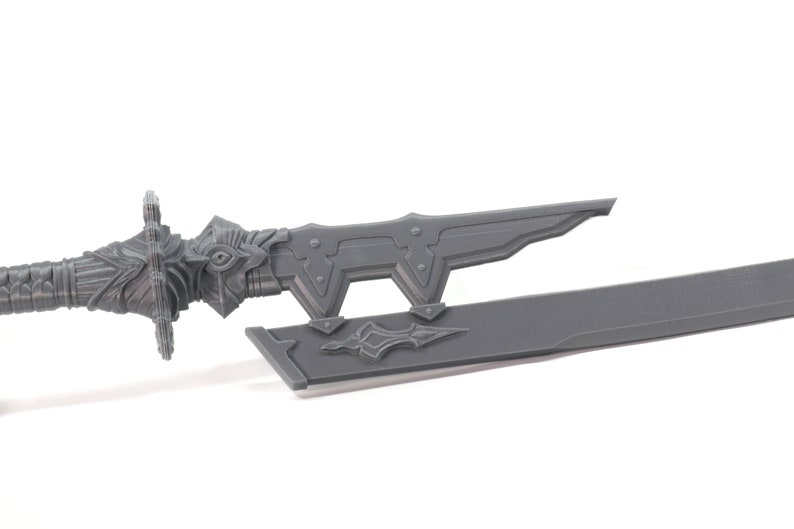 May include: A grey plastic sword with a detailed handle and a sharp blade. The sword is lying on a white surface.