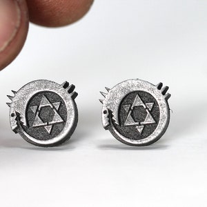 May include: A pair of silver earrings featuring a circular design with a black star of David and a snake wrapped around it.