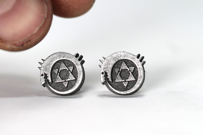 May include: A pair of silver earrings featuring a circular design with a black star of David and a snake wrapped around it.
