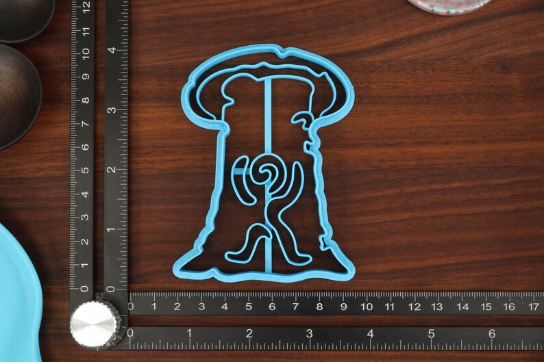 Puede incluir: Un cortador de galletas de pl&aacute;stico azul claro con forma de &aacute;rbol con un dise&ntilde;o en espiral en su interior. El cortador de galletas est&aacute; sobre una superficie de madera.