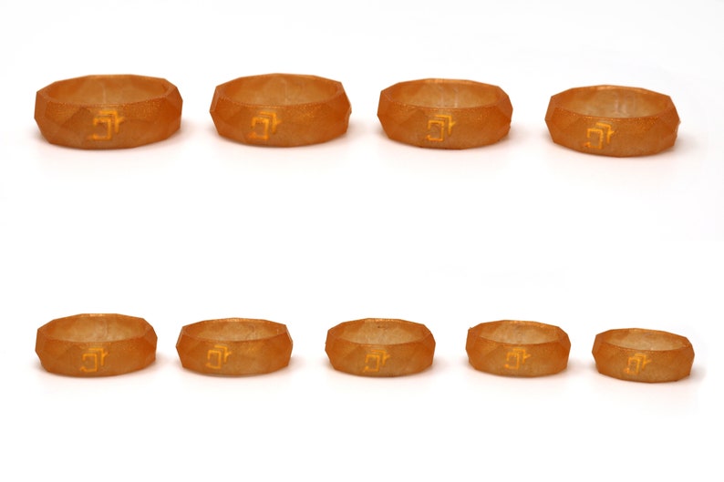 May include: Eight orange silicone rings with a geometric design and a gold inscription. The rings are arranged in two rows of four.