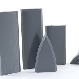 Puede incluir: Cuatro piezas impresas en 3D de color gris, incluyendo tres bloques rectangulares y una pieza puntiaguda. Los bloques son todos del mismo tama&ntilde;o y forma, mientras que la pieza puntiaguda es m&aacute;s peque&ntilde;a y tiene una punta afilada en la parte superior.