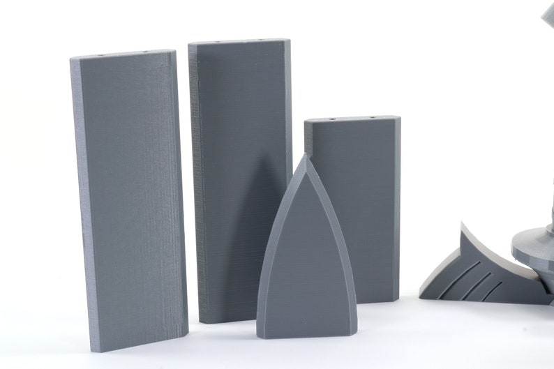 Puede incluir: Cuatro piezas impresas en 3D de color gris, incluyendo tres bloques rectangulares y una pieza puntiaguda. Los bloques son todos del mismo tama&ntilde;o y forma, mientras que la pieza puntiaguda es m&aacute;s peque&ntilde;a y tiene una punta afilada en la parte superior.