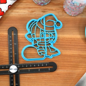 May include: Blue plastic cookie cutter shaped like a cartoon character wearing a Santa hat and holding a snowball.