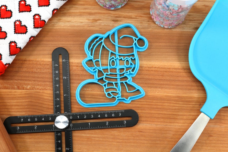 May include: Blue plastic cookie cutter shaped like a cartoon character wearing a Santa hat and holding a snowball.