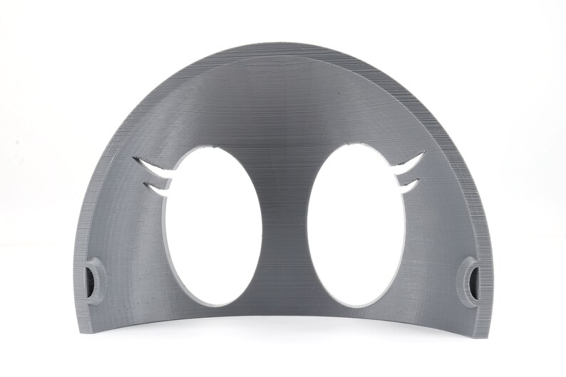 May include: A gray plastic 3D printed mask with two oval eye holes and a curved top. The mask has a textured surface and two small holes on the sides.
