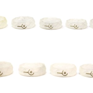 May include: Ten white silicone rings with a geometric design and a small symbol in the center. The rings are arranged in two rows of five.