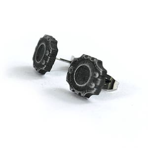 May include: A pair of silver stud earrings with a black, circular, detailed design. The earrings have a textured, antique-style finish.