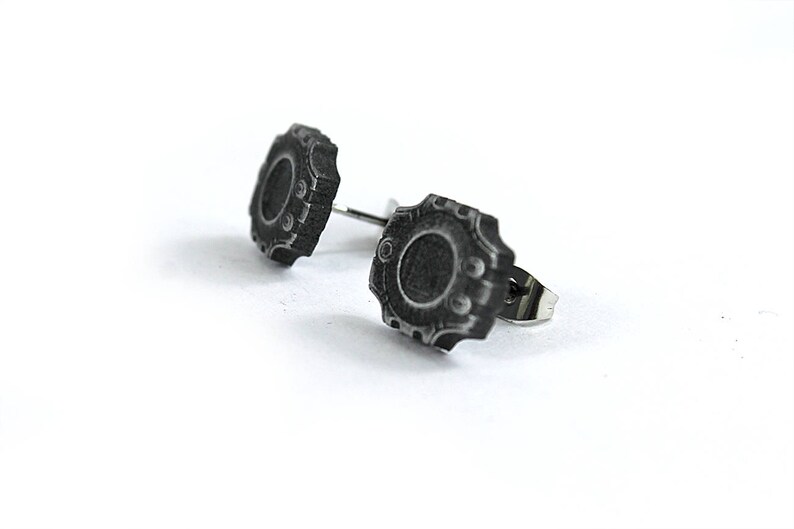 May include: A pair of silver stud earrings with a black, circular, detailed design. The earrings have a textured, antique-style finish.