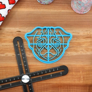 May include: A blue plastic cookie cutter shaped like a pug dog's face. The cutter has a grid pattern on the inside.